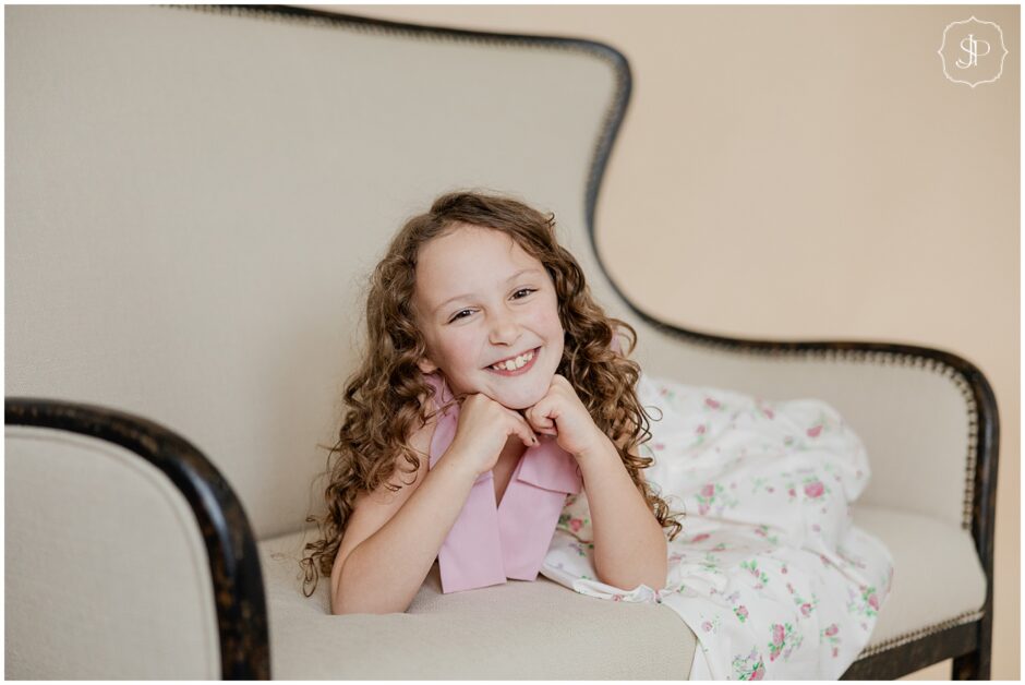 little girl smiling at the camera while lounging on a couch