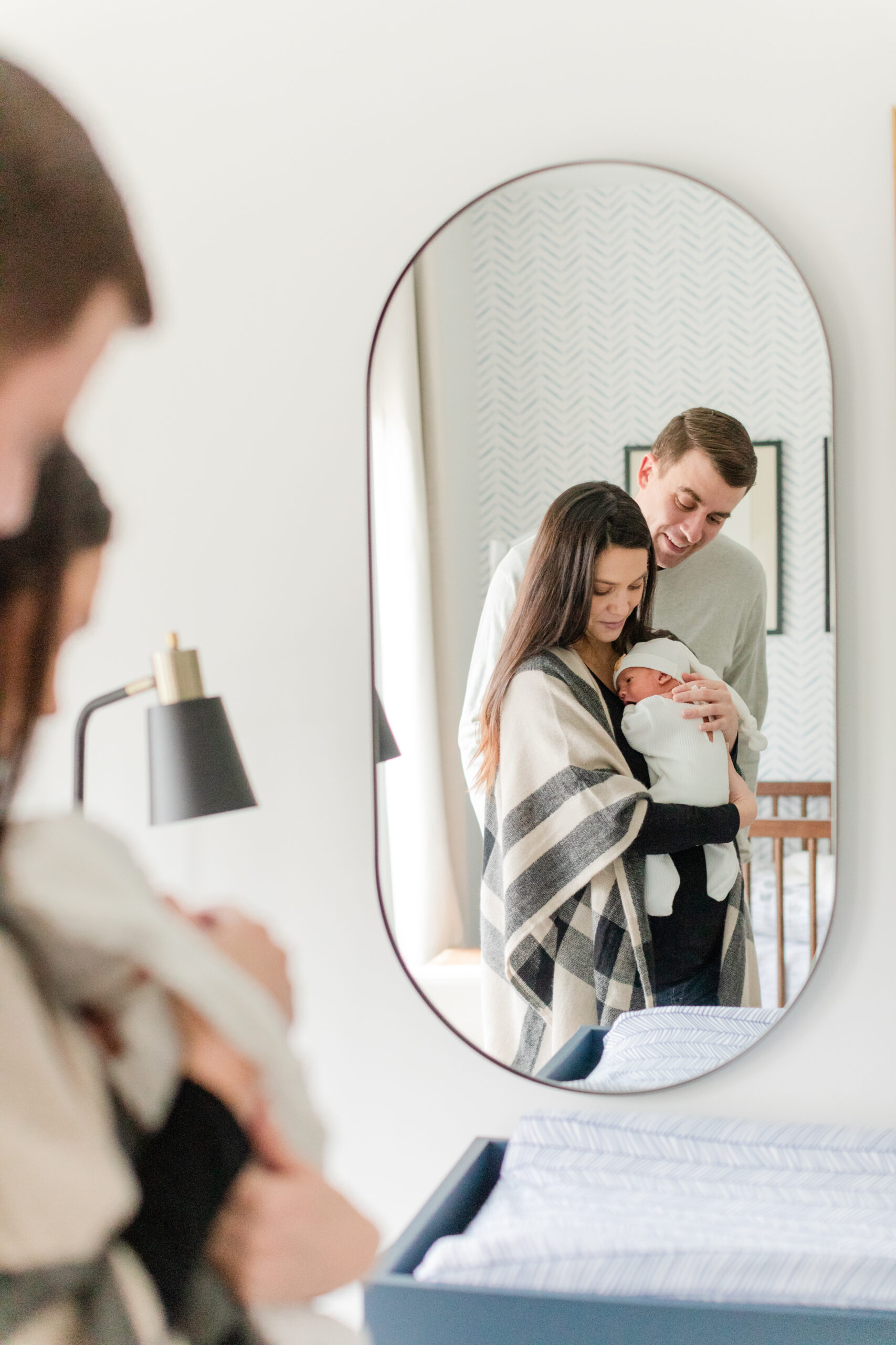 Mom and dad cuddled close holding their newborn baby in his nursery.