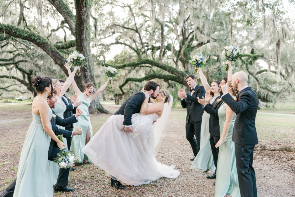 Bride and groom dipping for a kiss while their bridal party cheers them on in City Park Lousiana. 